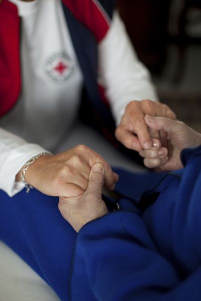Eine DRK Pflegerin und eine ältere Person fassen sich an den Händen. 