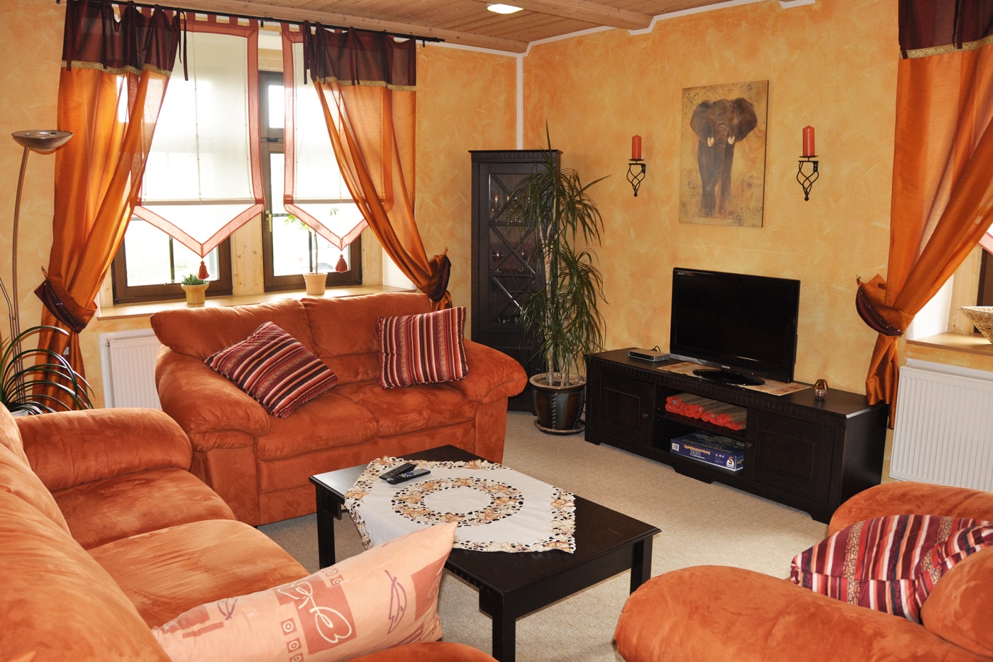 In einem hell gestrichenen Zimmer stehen dunkle Möbel und orange Sofas und Sessel. Die Einrichtung ist aufeinander abgestimmt und schafft ein gemütliches und warmes Ambiente.