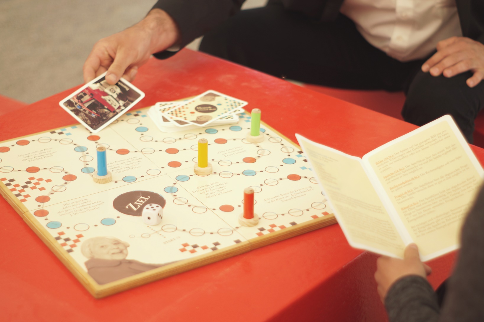 Zwei Personen spielen das DRK Brettspiel "Mensch erinner dich". Eine Person zieht eine Karte, die andere liest aus der Anleitung vor. Von beiden Personen sieht man nur die Hände.