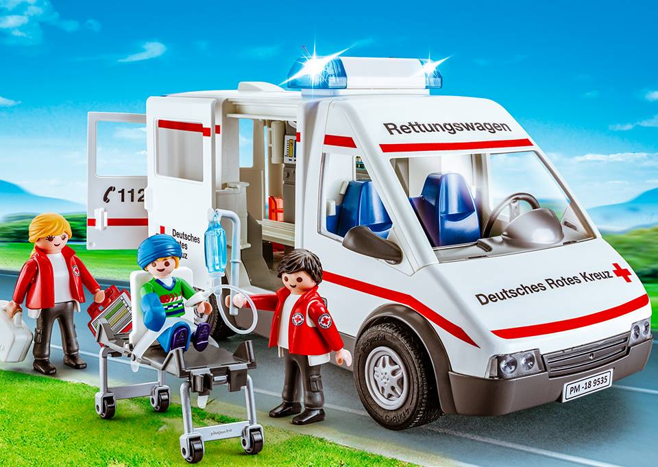 Ein Playmobil Rettungswagen, zwei Sanitäter, ein Verletzter, eine Liege sowie ein Infusionsbeutel sind abgebildet.
