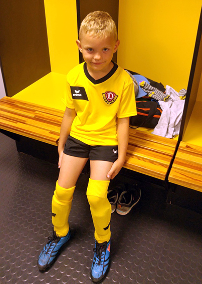 Ein Junge sitzt im Dynamo-Dresden-Trickot in der Umkleidekabine dieses Fußballvereins.
