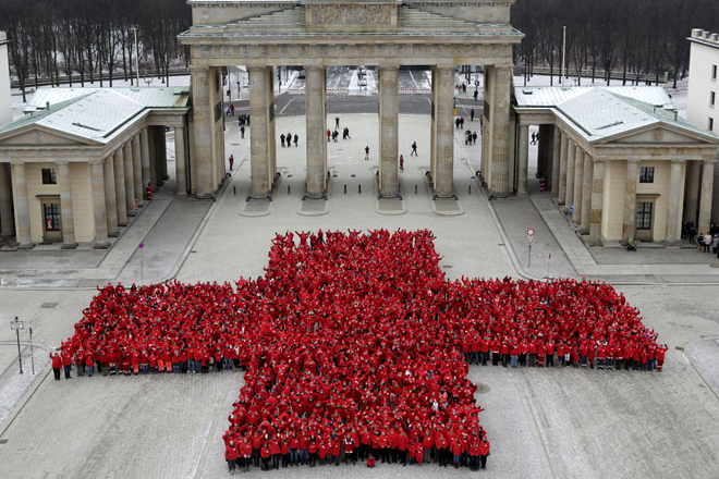 Ehrenamtliche des Deutschen Rotenkreuzes formieren sich vor dem Brandenburger Tor als riesiges Kreuz. Sie tragen rote Kleidung. Das Foto wurde von oben aufgenommen.