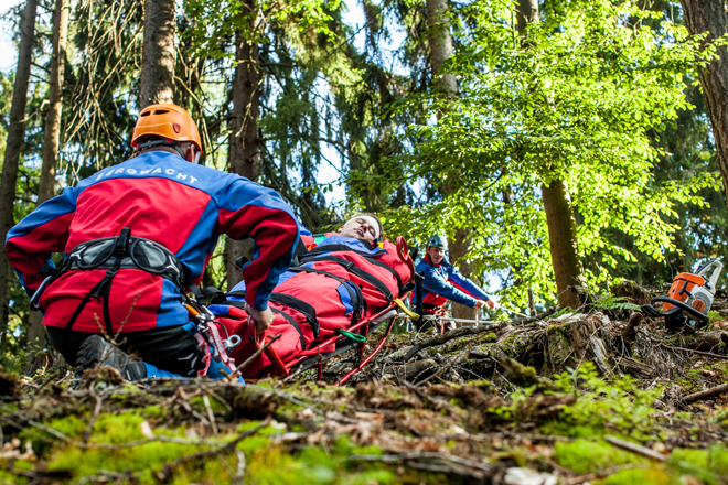 Ehrenamtliche der DRK Bergwacht führen eine Rettungsübung durch. Mehrere Ehrenamtliche erklettern einen steilen Berg in einem Wald.