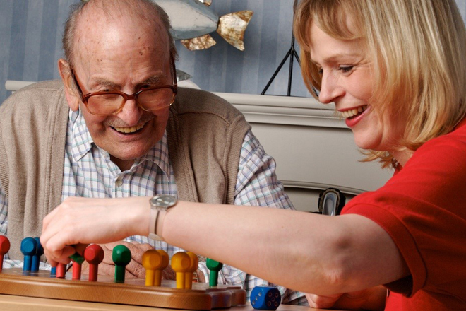 Ein Senior und eine Pflegerin spielen ein Brettspiel. Es scheint viel Spaß zu bereiten, denn beide lachen ausgelassen.