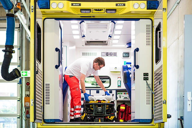 Ein junger Mann bereitet die Liege im Rettungswagen für den nächsten Patienten vor. Der Rettungswagen ist nun einsatzbereit und kann beim nächsten Notruf losfahren.