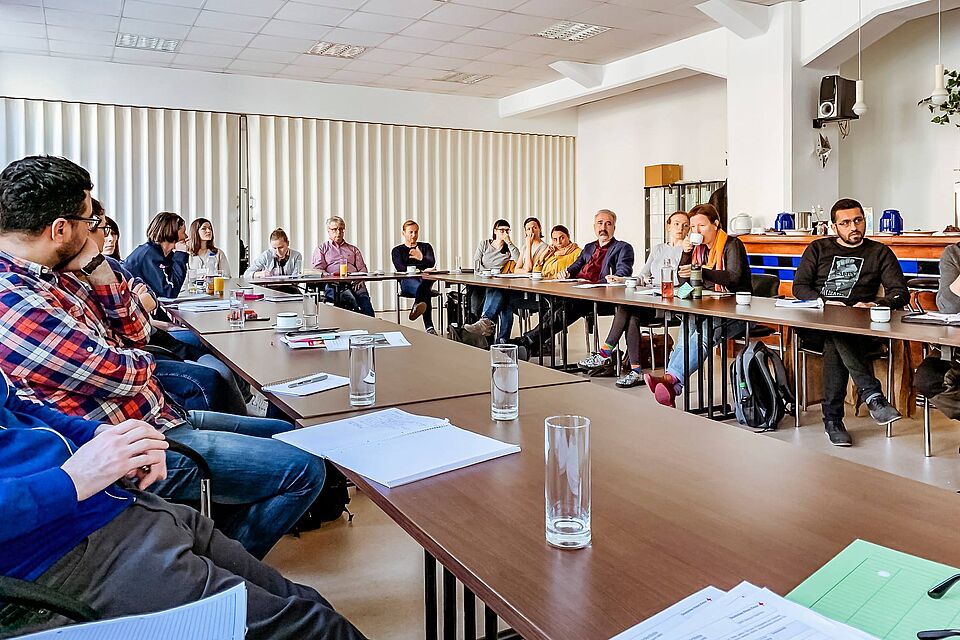 Leute sitzen bei einer Besprechung zum Thema digitaler Migrationsberatung in einem Raum zusammen.