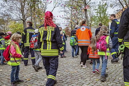 Mitarbeitende der Feuerwehr, des THWs und des Roten Kreuzes laufen gemeinsam mit den krebskranken Kindern in den Zoo.