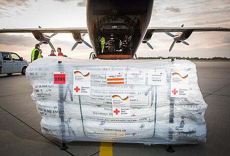 Eine Palette voller Zelte steht vor dem Frachtraum eines Flugzeugs auf der Landebahn.
