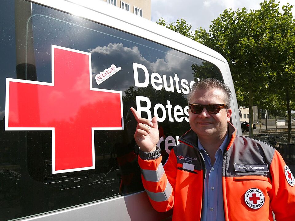Initiator der Kampagne #status6, Markus Kremser, steht vor dem DRK Einsatzwagen, der mit einem #status6-Aufkleber ausgestattet ist. 