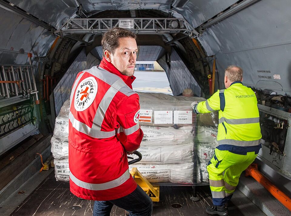 Ein Mitarbeiter des DRK und ein Mitarbeiter des Flughafens Dresden laden Kisten mit Zelten in den Frachtraum eines Flugzeugs.