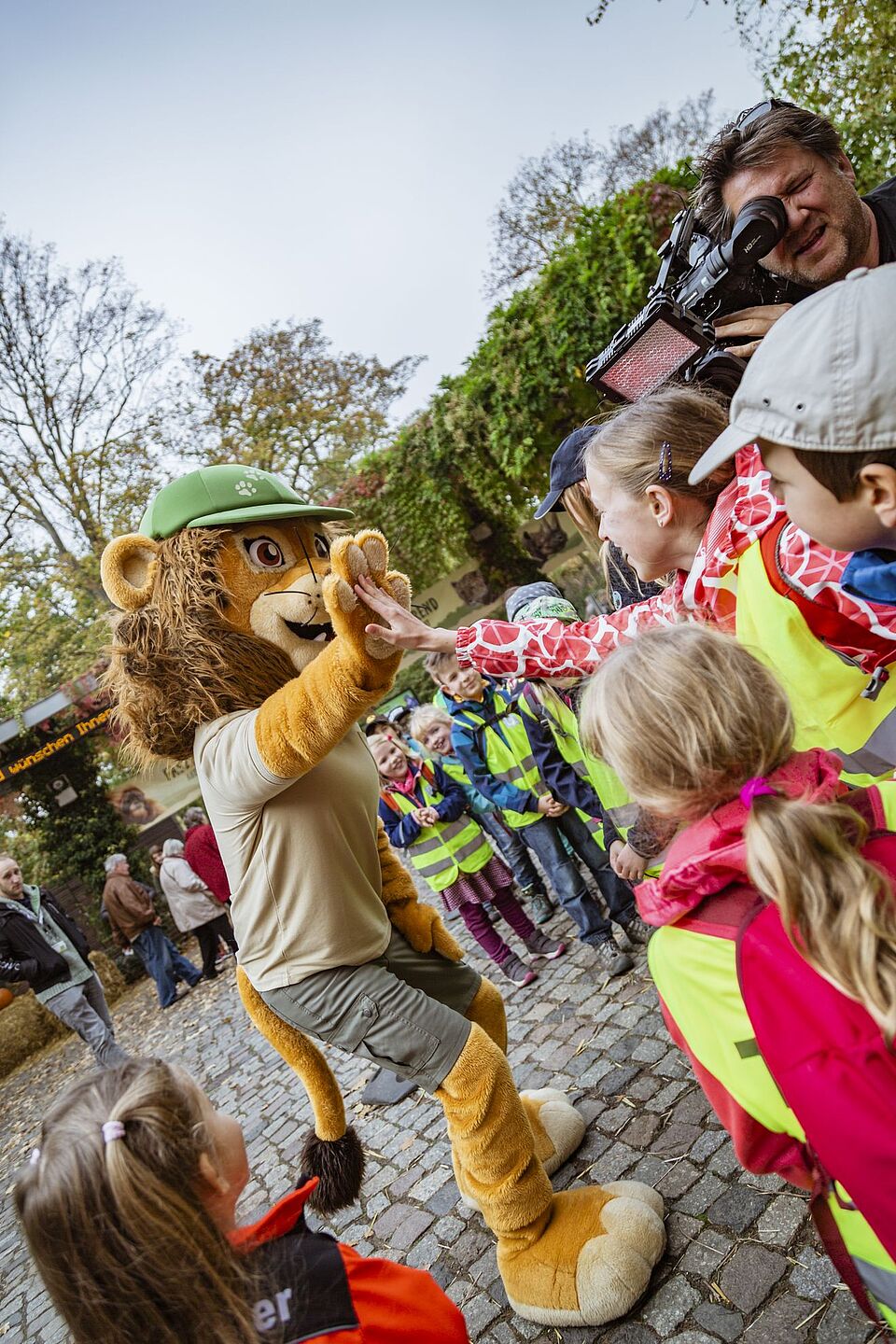 Das Maskottchen des Leipziger Zoos, ein Löwe in Tierpflegerbekleidung, klatscht mit den Kindern ab