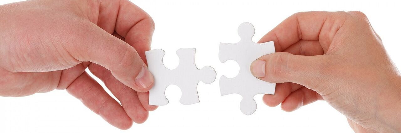 Zwei Hände halten je ein Puzzlestück, die zueinander passen und ein Teil ergeben.