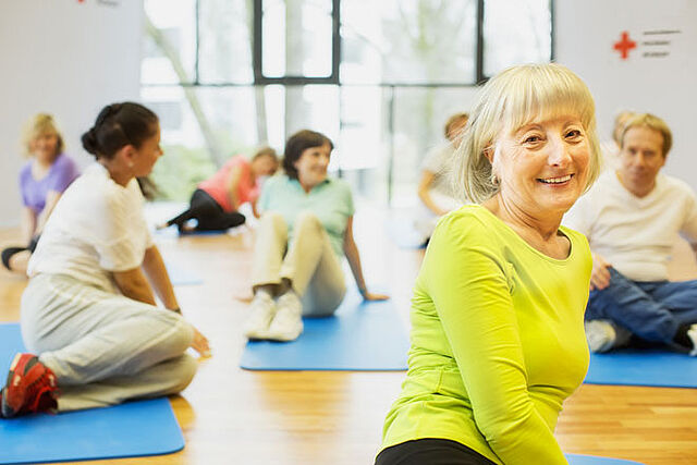 Mehrere Senioren sitzen auf Fitnessmatten auf dem Fußboden und machen Übungen, um fit zu bleiben.