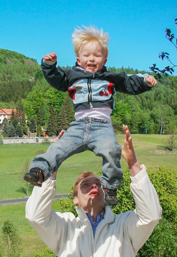 Vater-Kind-Kur Ein Vater wirft sein Kind in die Luft und fängt es wieder auf. Beide lachen.