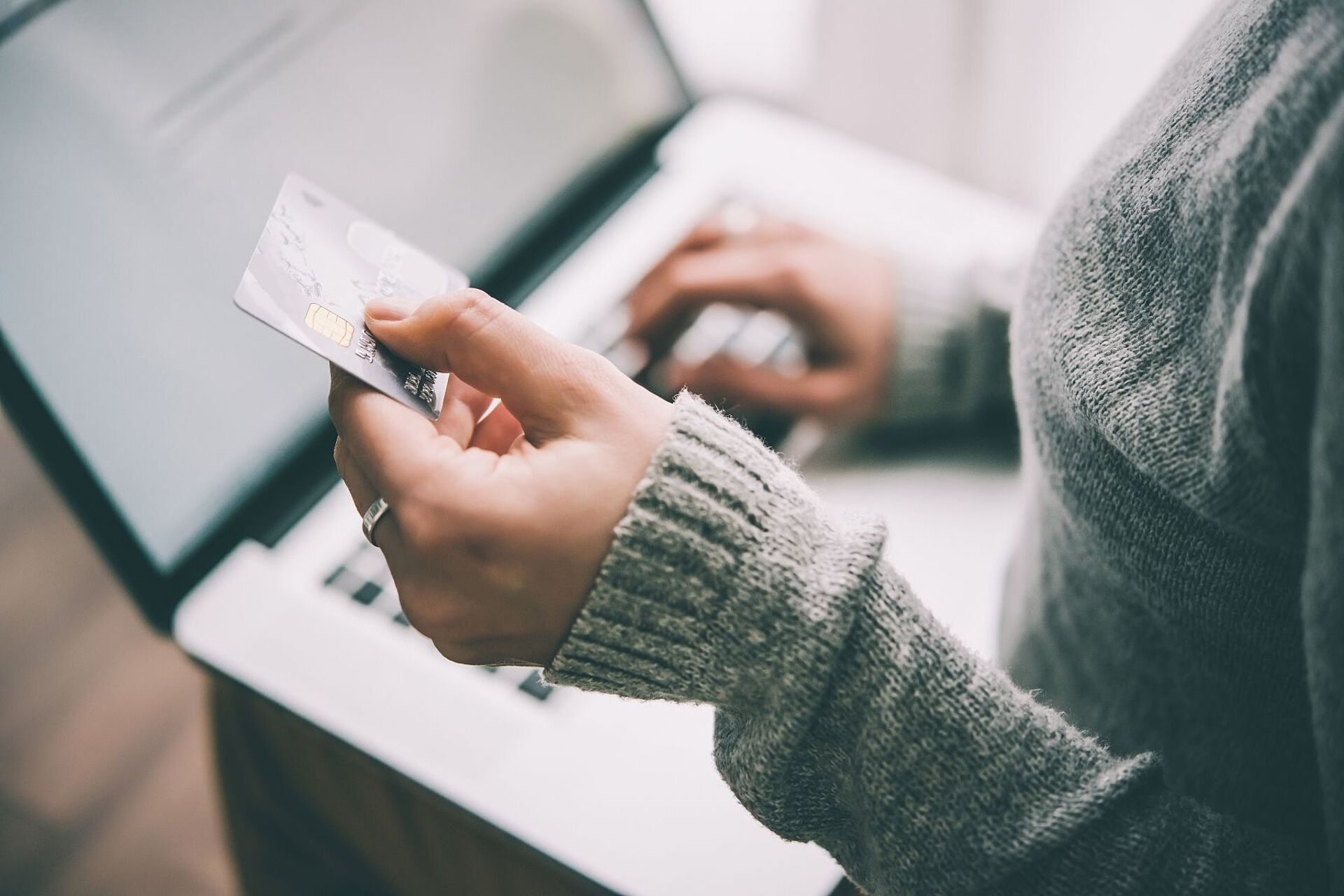 Eine Frau sitzt an ihrem Laptop und hält ihre Bankkarte in der Hand. Sie tippt ihre Kontodaten ab.
