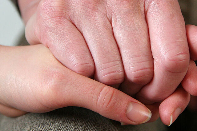 Eine Hand legt sich beruhigend auf eine andere, faltige Hand. Die Geste drückt Vertrauen und Unterstützung aus.