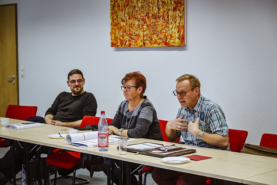Mitwirkende des Fachtages Suchdienstbasisstellen sitzen an ihren Tischen und lauschen dem Vortragenden