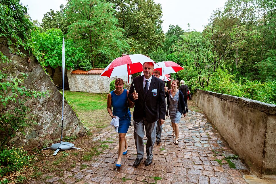 Einige Gäste laufen den Weg zum Schloss mit einem DRK Regenschirm, weil es zu Beginn stark regnet.
