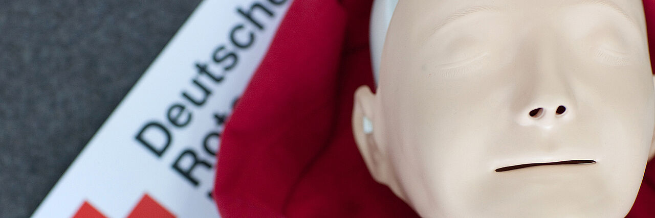 Der Kopf einer Erste-Hilfe-Puppe ist zu sehen. Die Puppe liegt auf einer DRK Decke auf dem Boden.