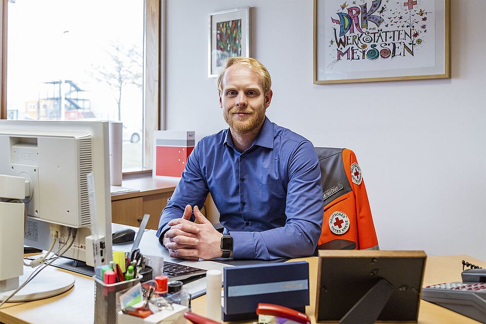 Der Werkstattleiter der Werkstätten für Menschen mit Behinderung Meißen sitzt in seinem Büro am Schreibtisch und schaut in die Kamera.