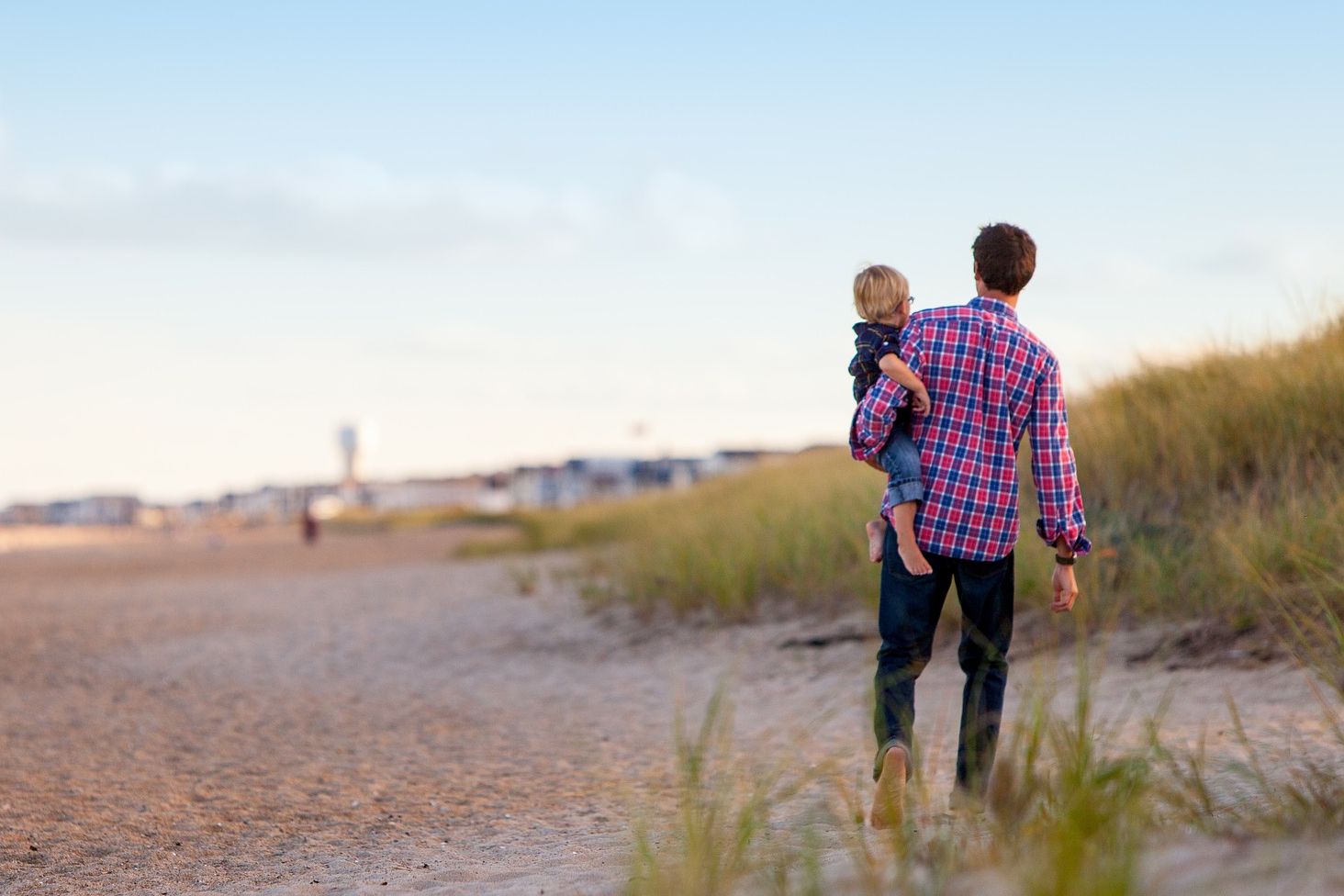 Ein Mann steht mit einem Kleinkind auf dem Arm am Strand und schaut in die Ferne.