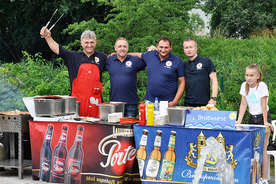 Vier Männer stehen am Grill und kümmern sich um die hungrigen Gäste.