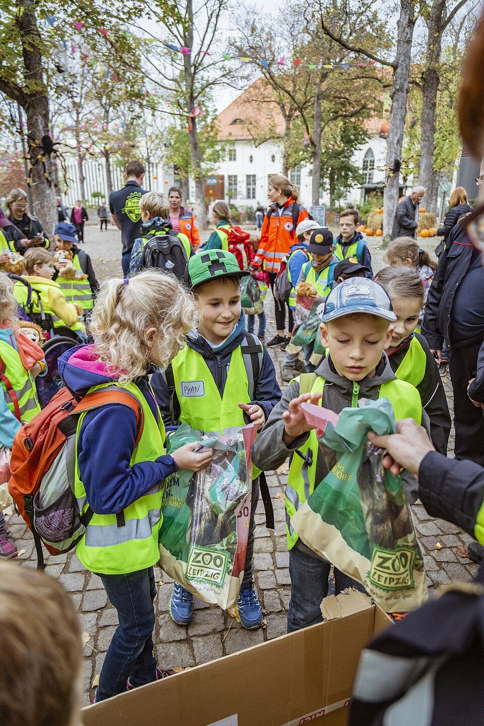 Ein Mädchen und zwei Jungen holen sich ihre Zoo-Leipzig-Tüte mit kleinen Geschenken ab