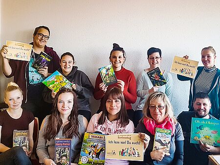 Zehn junge Frauen und Männer schauen in die Kamera und halten Kinderbücher in den Händen. Am Vorlesetag lesen sie in einer Schule daraus vor.